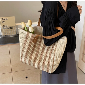 Close-up of handmade woven straw tote bag with brown leather straps and striped pattern