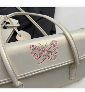 Detail shot of delicate pink butterfly embroidery on a cream PU leather shoulder bag