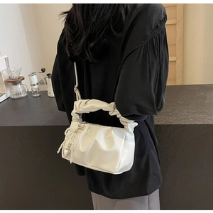 Detail of a creamy white pleated cloud bag featuring pearl bow and heart metal charms