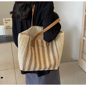 Detail view of woven straw tote bag with vertical stripes and leather handles worn by model