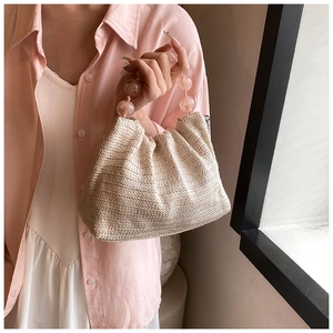 Gros plan sur la texture en paille tressée et la poignée élégante en perles roses du sac