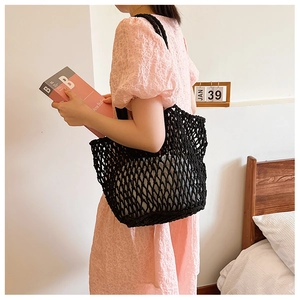 Close-up of black hand-crocheted woven mesh tote bag styled with a pink lace dress