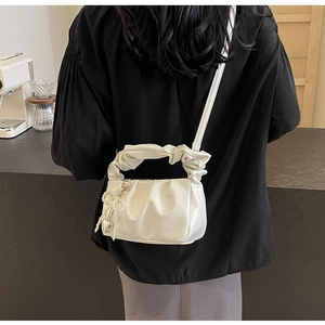 Back view of a white pleated cloud bag with pearl bow charm and twisted handle on a model