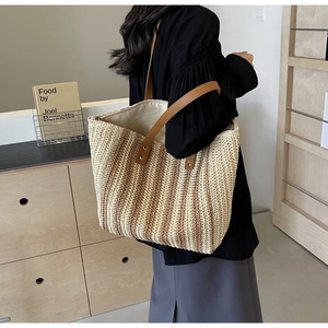 Detail of large woven straw tote bag with brown leather handles worn by a model