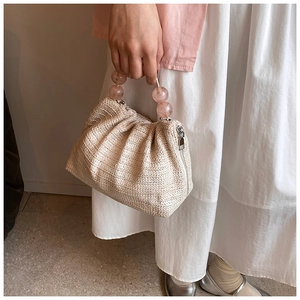 Détail du sac bandoulière en paille beige avec poignées en perles roses et zip métallique