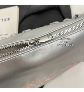 Detail of silver metallic PU handbag showing smooth metal zipper and pink embroidery