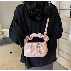 Detail of pink PU crossbody bag with ruffled handle and pearl bow charm on model