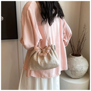 Détail d'un sac bandoulière en paille beige avec poignée en perles roses et chaîne