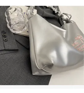 Detail of silver PU leather handbag featuring a pink bow and stylish ruched handle design