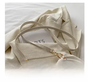 Detail view of cream crossbody bag featuring a marble-textured pearl strap and gold hardware