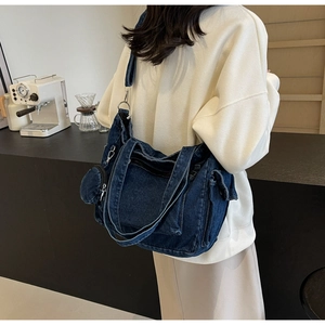 Detail of blue denim crossbody bag showing side pockets and removable coin pouch pendant