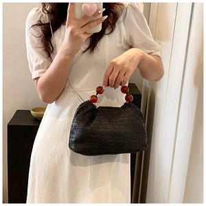 Détail du sac bandoulière en paille noire avec anse en perles ambrées sur un modèle