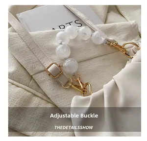 Close-up of cream pleated cloud bag featuring pearl handle and adjustable golden buckle