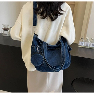 Detail of blue denim canvas tote bag with round coin purse charm on a model's shoulder