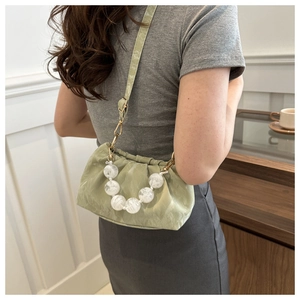 Close-up of light green pleated crossbody bag with large white beaded chain accessory