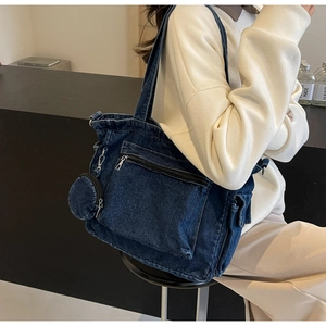 Detail of a large denim tote bag with functional zip pockets and round coin purse charm