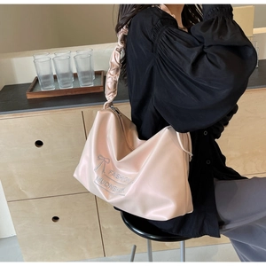 Detail of light pink glossy PU tote bag featuring a silver bow print and ruched shoulder strap