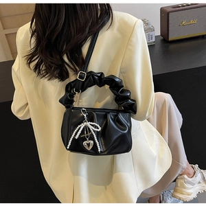Detail of black pleated faux leather bag with pearl bow and metal heart charm on a shoulder strap