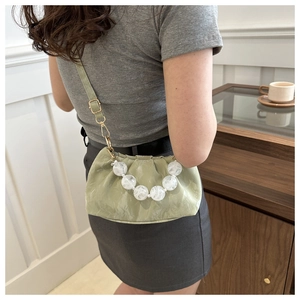 Detail of light green pleated cloud bag featuring white marble decorative beads and strap
