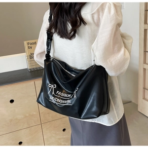 Model wearing large black PU leather shoulder bag with white fashion print and bow design