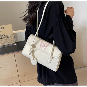 Detail view of cream white PU handbag featuring pink butterfly embroidery and heart charm