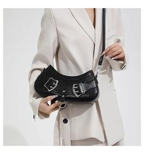 Detail of a black half-moon PU crossbody bag with silver buckles on a cream blazer