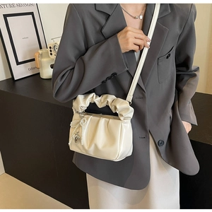 Detail of creamy white pleated handbag featuring pearl bow and metallic heart charms