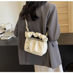 Beige cloud pleat handbag worn as a crossbody bag shown on model in a cafe setting