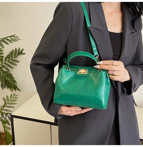 Detail of vintage green leather handbag featuring golden twist lock and top handle grip