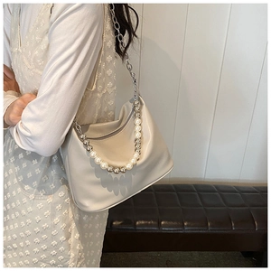 Dettaglio borsa hobo beige con tracolla di perle e catena d'argento su una panca in pelle