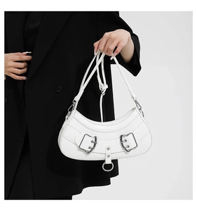 Close-up of white crescent bag with silver buckles held by a model in a black blazer