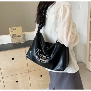 Detail view of black PU leather tote bag with gathered strap and bow print worn by a model