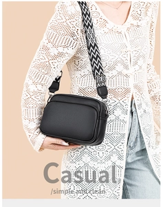 Detail of black pebbled leather crossbody bag with geometric wide woven strap worn by model