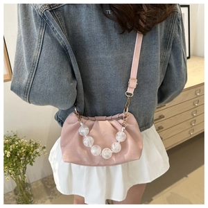 Detail view of pink pleated handbag with acrylic bead handle on a model's shoulder