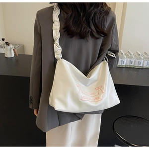 Detail of white PU leather crossbody bag with ruffle strap and pink bow design