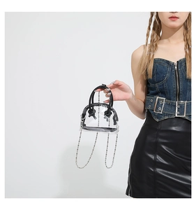 Détail d'un sac à main semi-circulaire en PVC transparent avec poignées noires et chaîne