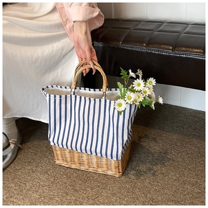 Detail of a blue striped straw tote bag with round handles held by a model on a leather stool