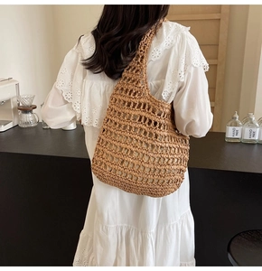 Close-up of handmade brown straw woven mesh bag with hollow structure on white lace dress