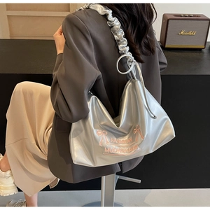 Detail shot of a silver metallic crossbody bag featuring a pink bow and ruched handle design