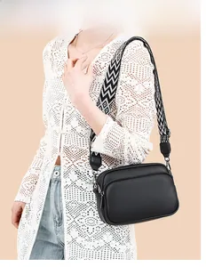 Detail of black pebbled leather crossbody bag featuring a wave pattern wide strap