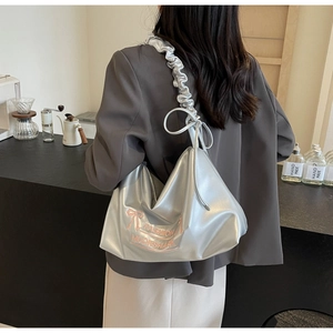 Silver pleated cloud bag with pink bow detail worn by a model in a cafe setting