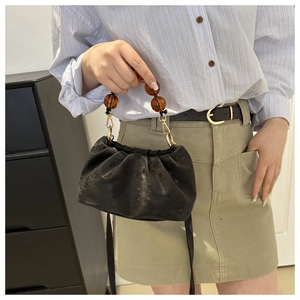 Close-up of black metallic textured cloud bag with amber beaded handle and gold hardware