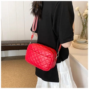 Close-up of red quilted crossbody bag with wide patterned strap and metal hardware