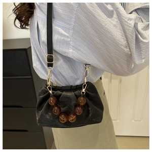 Detail of black pleated cloud bag featuring amber resin beads and adjustable shoulder strap