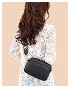 Detail of black pebbled leather crossbody bag with geometric jacquard wide strap on model
