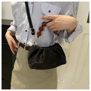 Detail of black pleated crossbody bag with amber resin bead handles and gold hardware