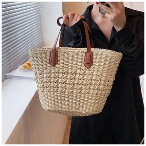 Détail d'un sac cabas en paille tressée avec poignées en cuir marron porté par un modèle