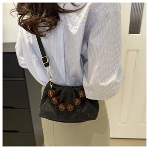Detail of black pleated mini bag with amber beads and adjustable thin shoulder strap