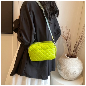 Detail of neon green quilted crossbody bag with stylish geometric wide strap on model