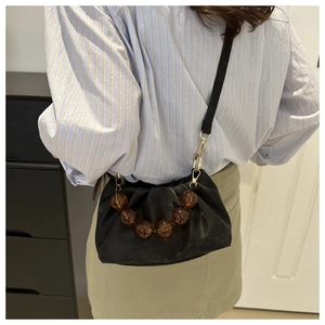 Detail of black pleated cloud bag featuring amber bead accents and a slim shoulder strap